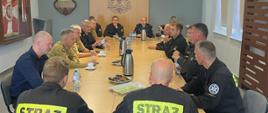 Strażacy siedzą za stołem podczas spotkanie z kierownictwem Państwowej Straży Pożarnej.