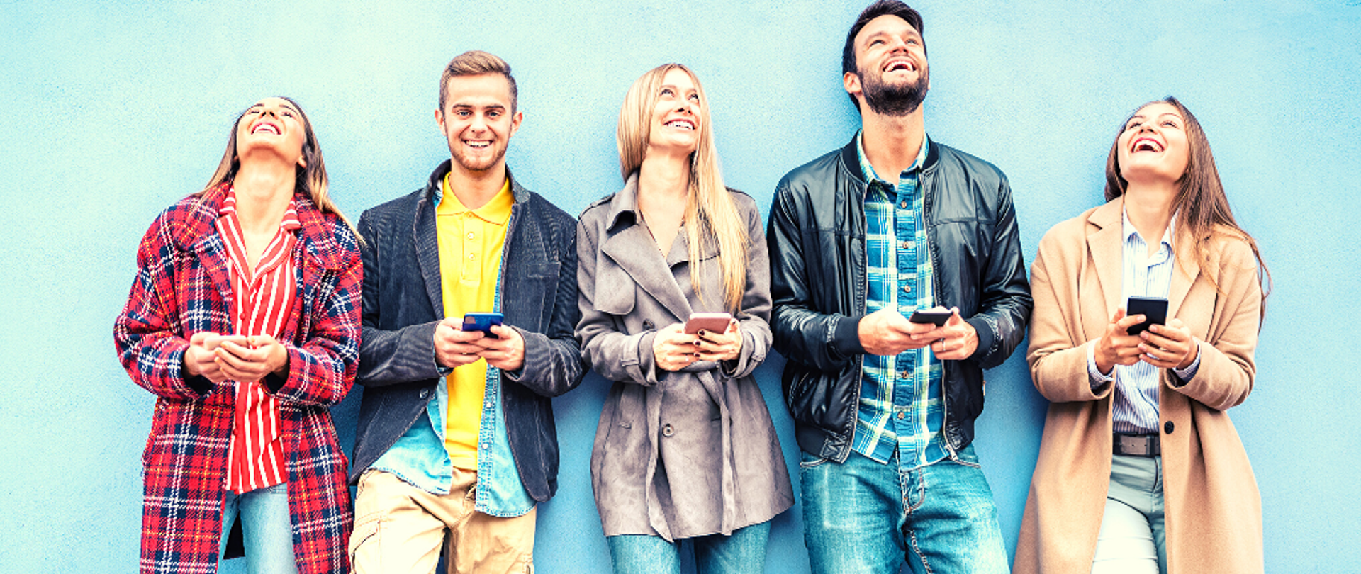 Zdjęcie przedstawiające piątkę uśmiechniętych, młodych osób trzymających smartfony. 