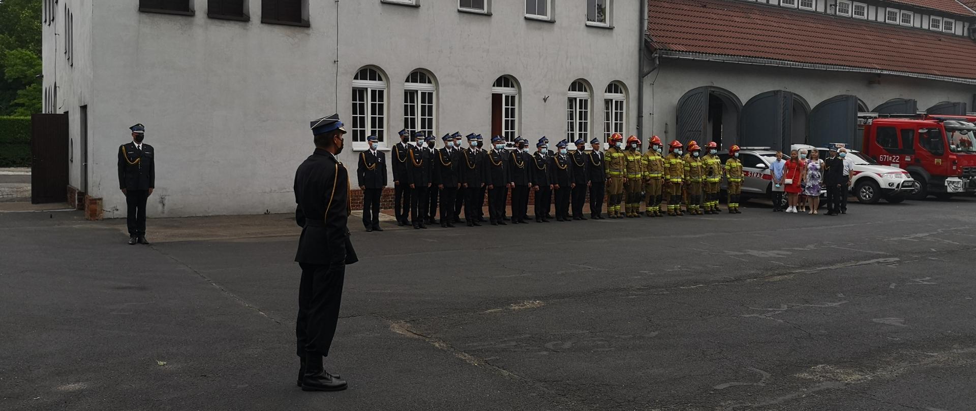 Uroczysta zbiórka z okazji zakończenia służby przez ogniomistrza Manfreda Świętka przed Komendą Miejską Państwowej Straży Pożarnej w Zabrzu. Przed budynkiem komendy stoją w dwuszeregu funkcjonariusze zabrzańskiej straży pożarnej. 