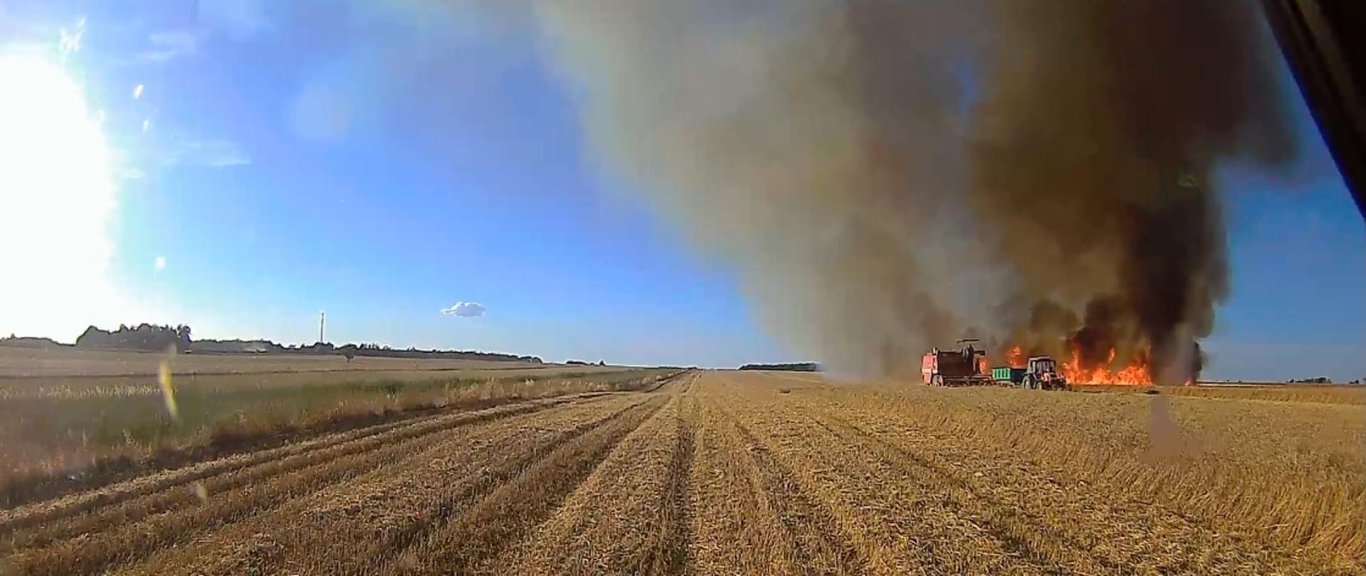 Ujęcie z pojazdu pożarniczego podczas dojazdu do pożaru zboża. Kombajn i ciągnik na polu. 