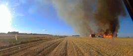 Ujęcie z pojazdu pożarniczego podczas dojazdu do pożaru zboża. Kombajn i ciągnik na polu. 