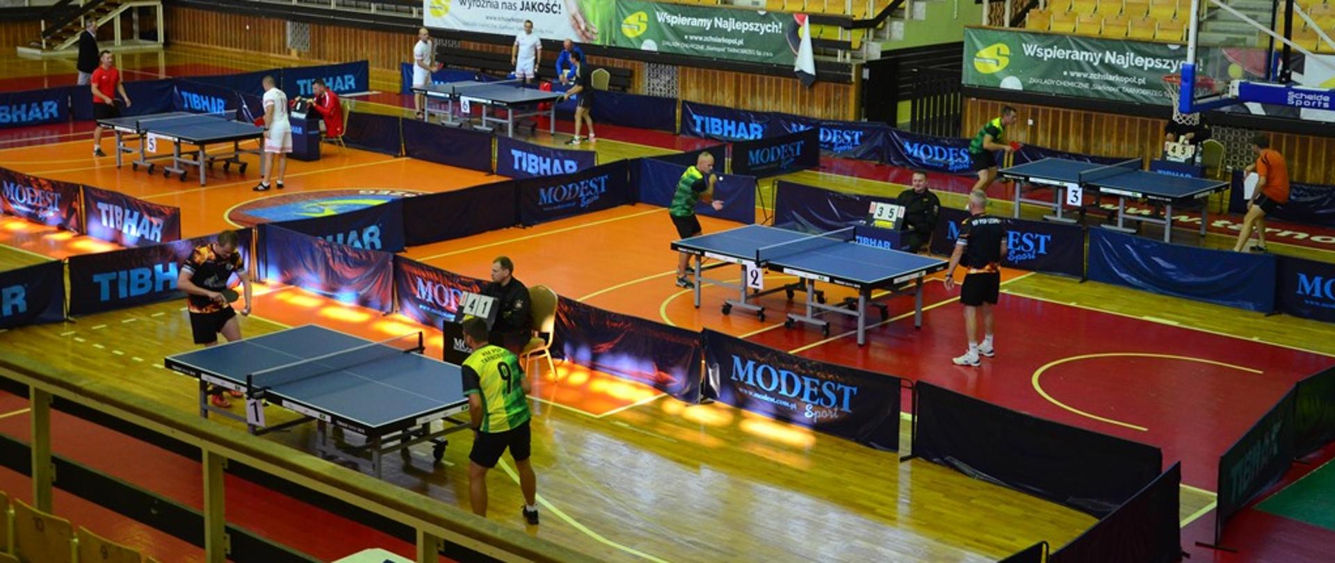 Na hali sportowej widoczne rozgrywki w tenisie stołowym.