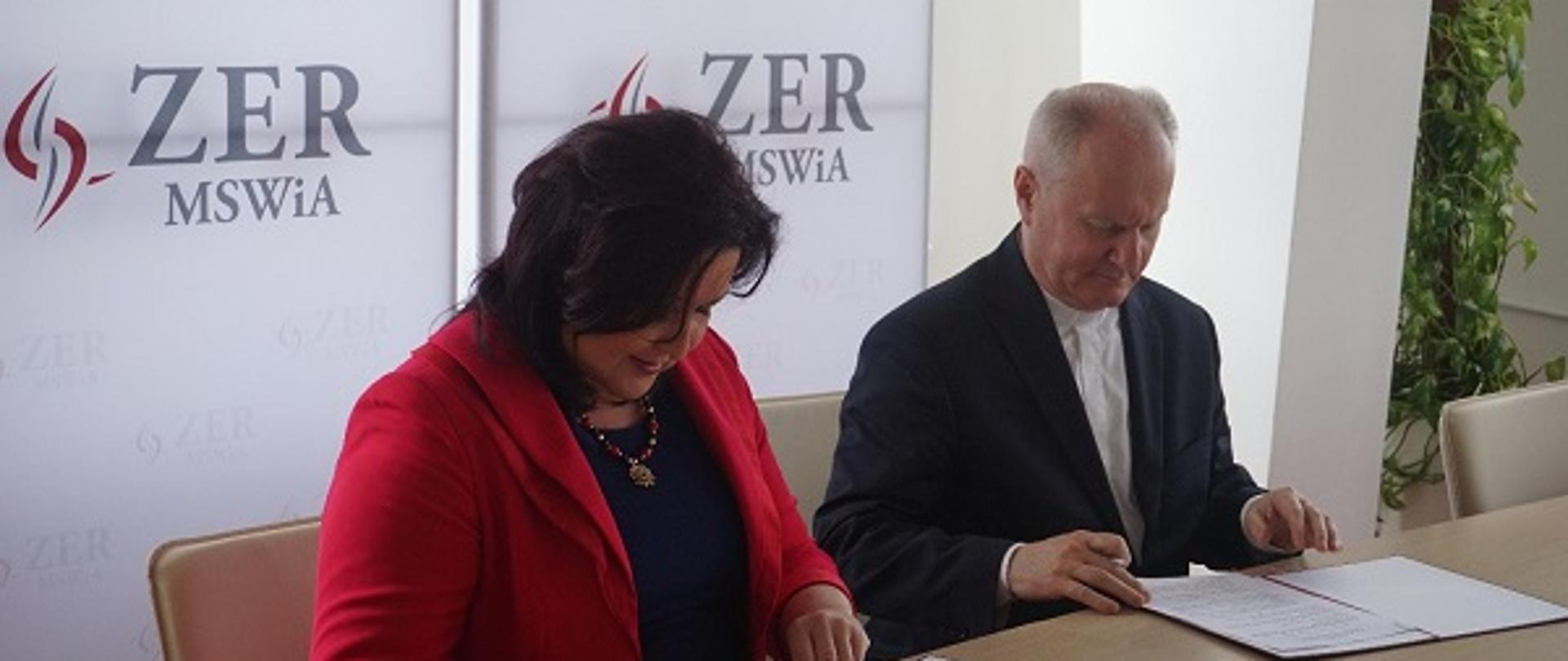 Na zdjęciu jest Pani Małgorzata Zdrodowska, Dyrektor Zakładu Emerytalno-Rentowego Ministerstwa Spraw Wewnętrznych i Administracji oraz ksiądz prof. dr hab. Mirosław Kalinowski, Rektor Katolickiego Uniwersytetu Lubelskiego Jana Pawła II w Lublinie, którzy podpisują porozumienie o współpracy. W tle widać logo ZER MSWiA.
