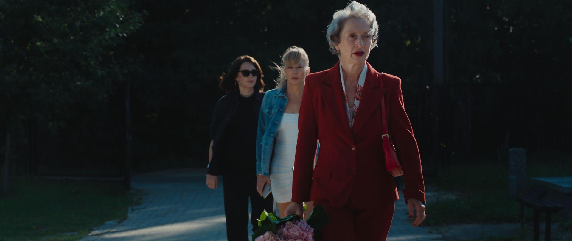 Trzy kobiety idą alejką jedna za drugą, pierwsza trzyma bukiet hortensji