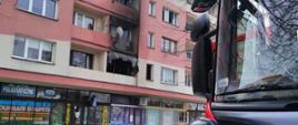 na pierwszym planie widać przód pojazdu gaśniczego, na drugim planie widać okopconą elewację bloku nad oknami jednego z mieszkań