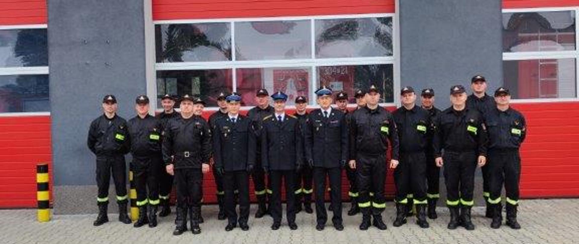 Zdjęcie przedstawia funkcjonariuszy uczestniczących w pożegnaniu emeryta stojących na tle budynku Jednostki Ratowniczo-Gaśniczej Numer 4 w Chmielniku.