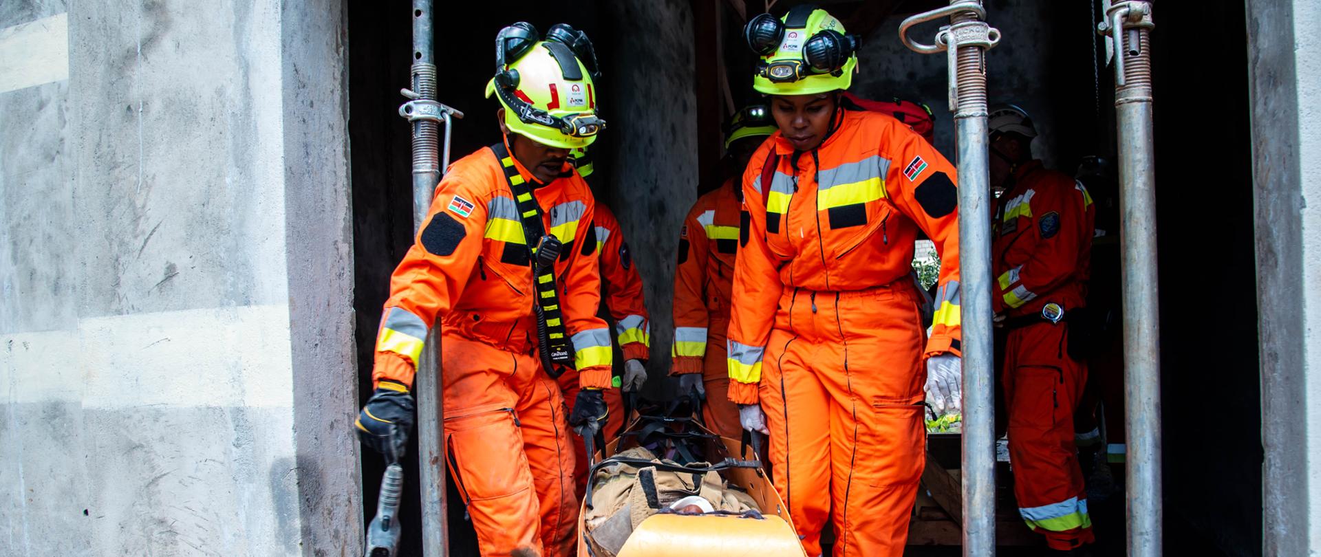 Kobieta i mężczyzna w strojach strażaków wynoszą rannego na noszach
