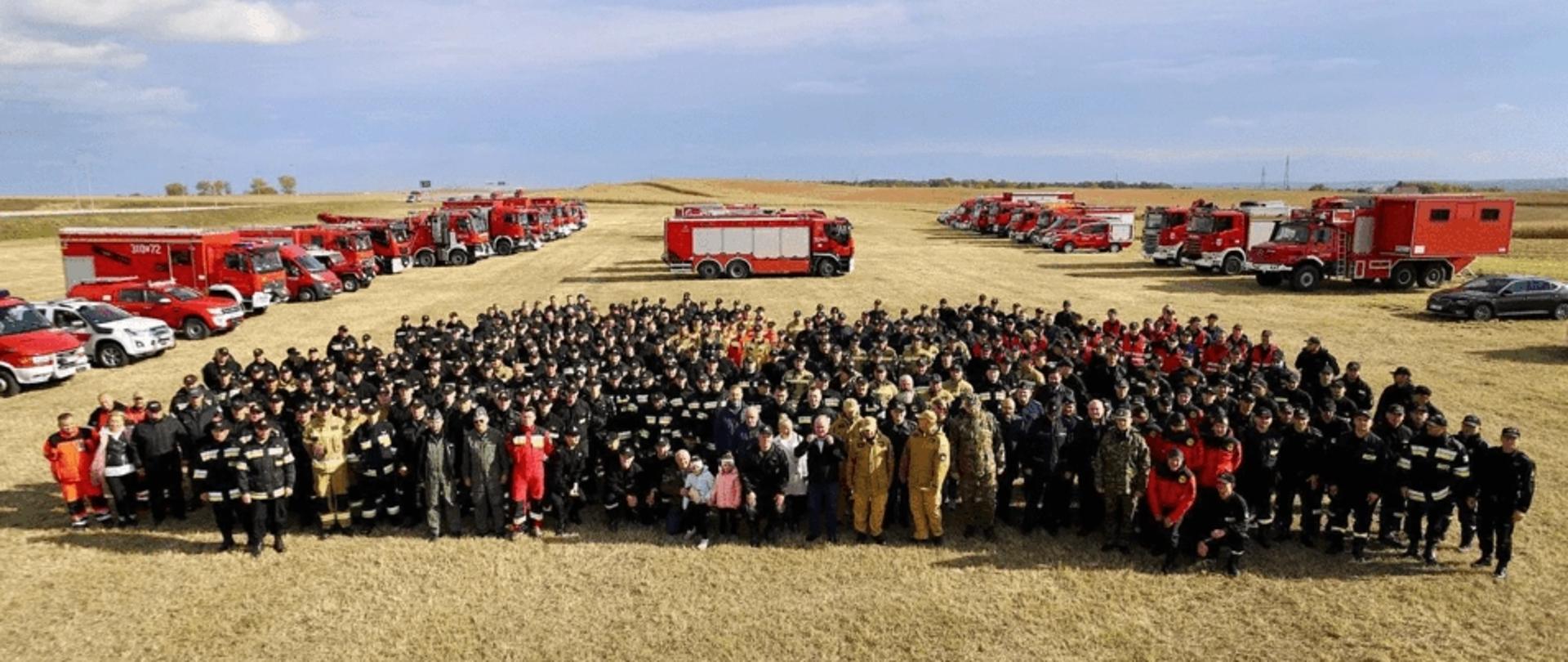 Udział szkolnego odwodu operacyjnego Komendanta Głównego PSP w ramach ćwiczeń "Opolskie 2021" - zdjęcie wszystkich uczestników ćwiczeń, w tle samochody