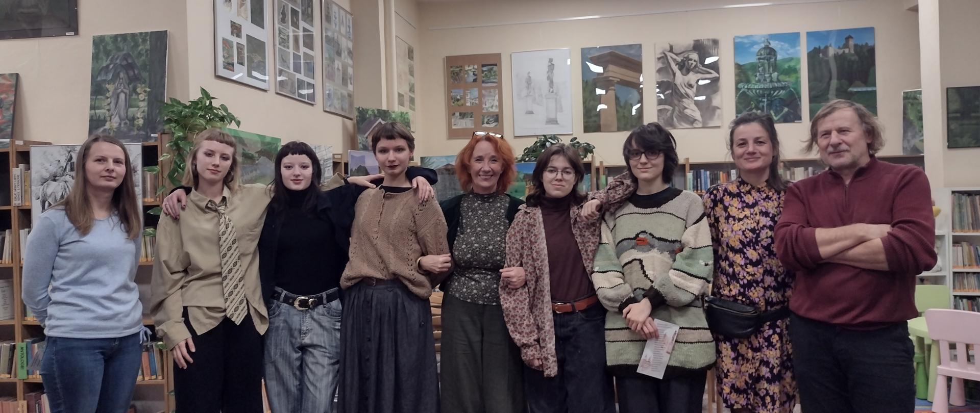 We wnętrzu biblioteki stoi grupa pięciu dziewcząt i czwórki dorosłych pozując do zdjęcia