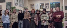 We wnętrzu biblioteki stoi grupa pięciu dziewcząt i czwórki dorosłych pozując do zdjęcia