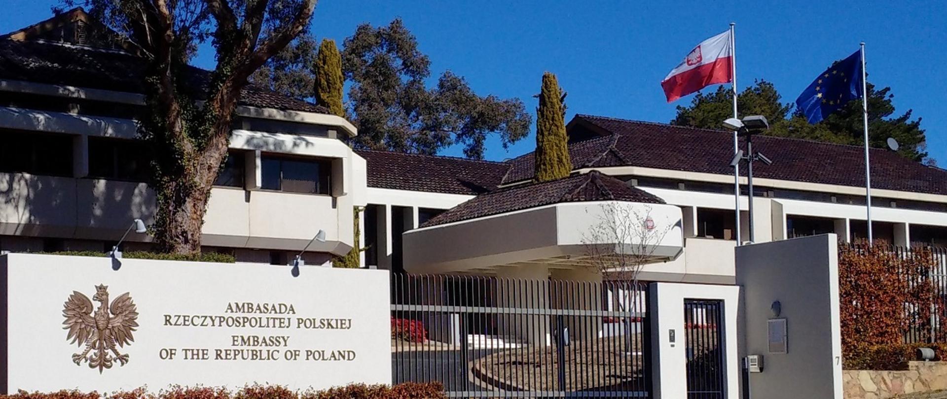 Zdjęcie przedstawia budynek Ambasady RP w Canberze, na froncie flaga Polski i Unii Europejskiej.
