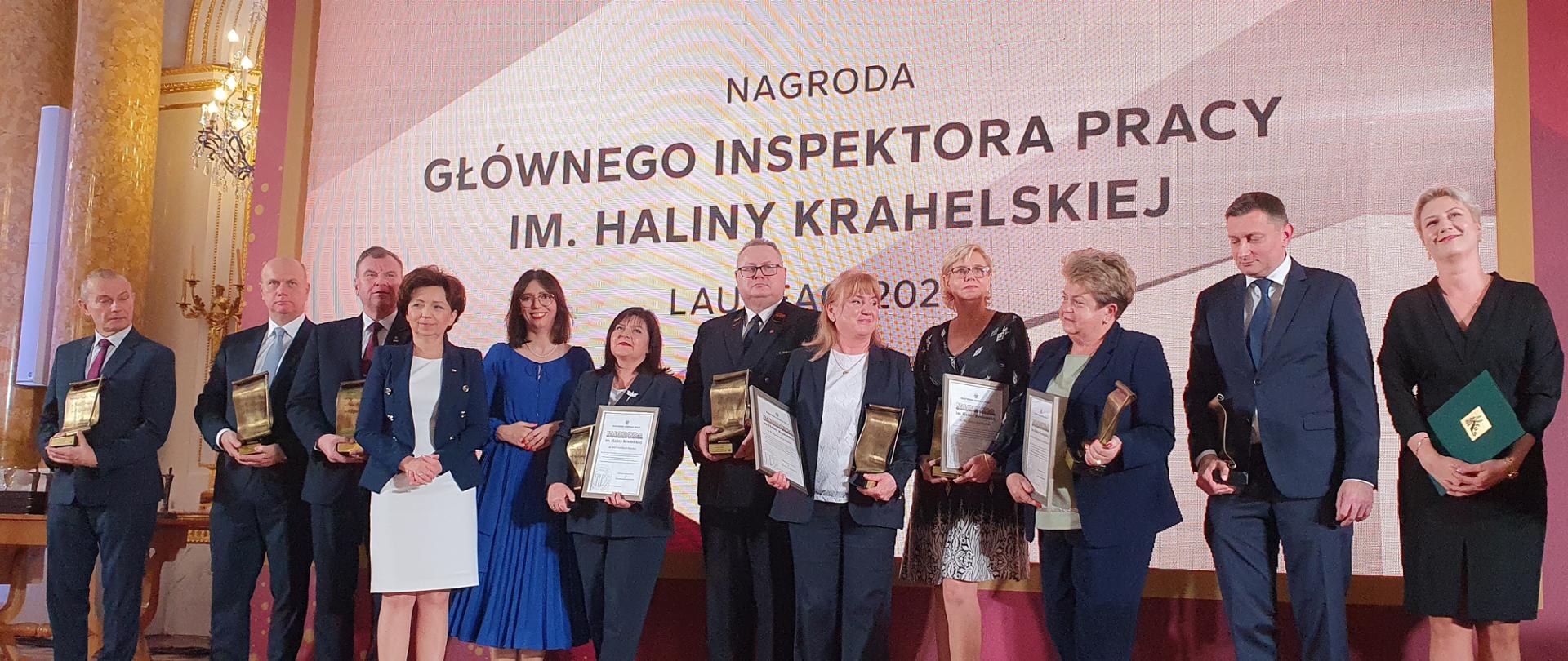 Laureaci nagrody Głównego Inspektora Pracy im. Haliny Krahelskiej trzymający wyróżnienia i otrzymane statuetki. Ubrani w eleganckie stroje.