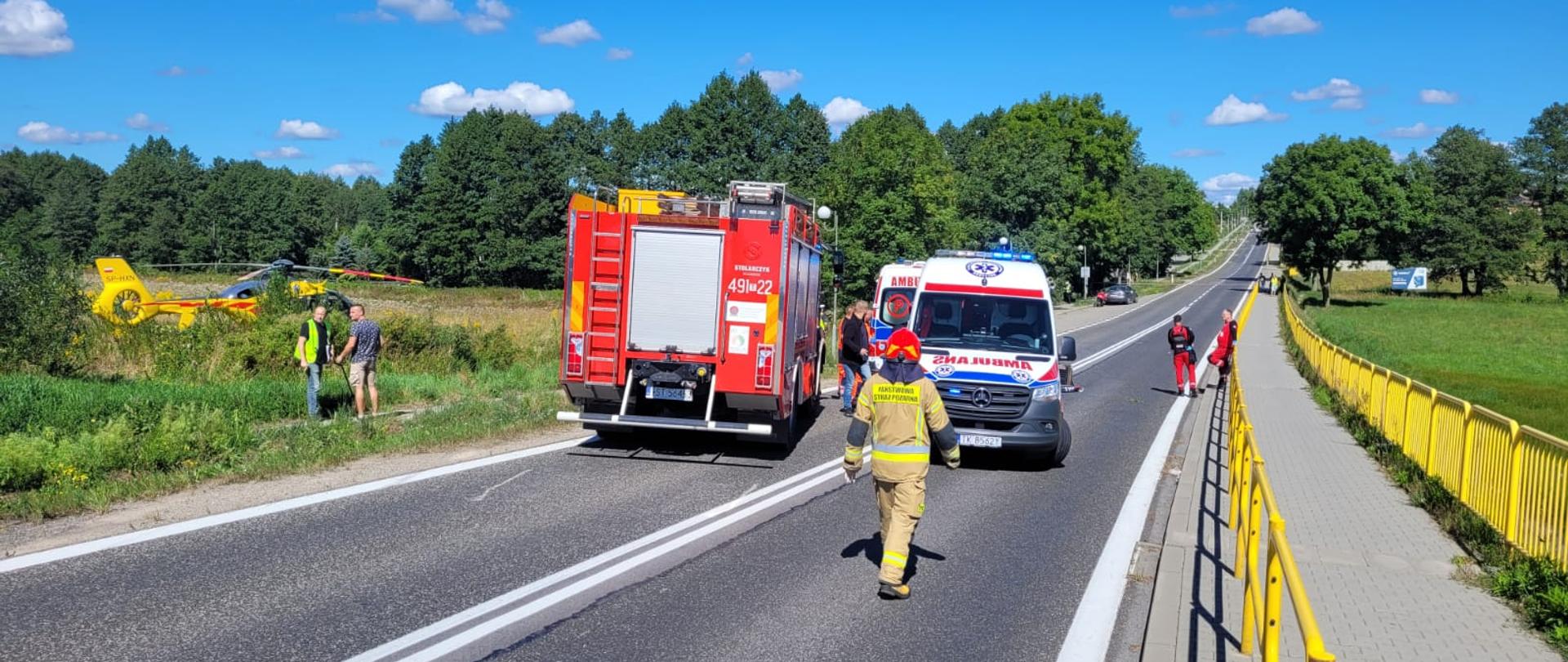 Samochód pożarniczy 2 karetki na jezdni drogi krajowej nr 9 , po lewej stronie poza jezdnią śmigłowiec LPR