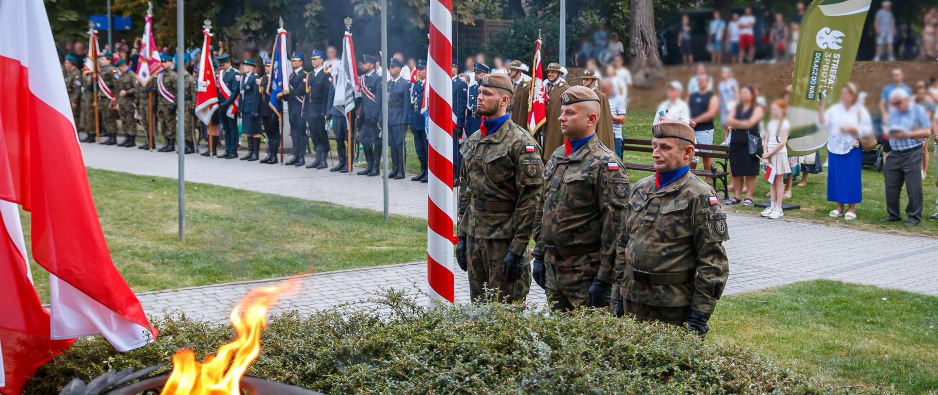 Uczestnicy uroczystości zgromadzeni wokół pomnika. Zapalony znicz