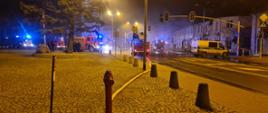 Na zdjęciu widać samochody ratowniczo gaśnicze podające wodę na płonące budynki.