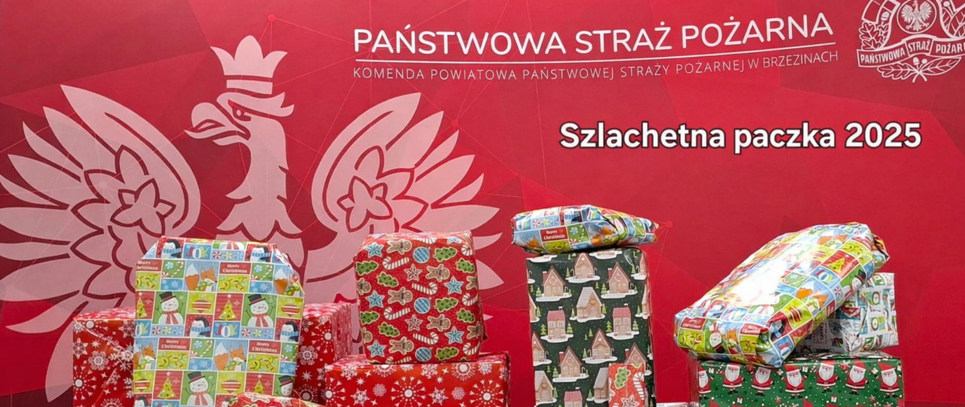 Na tle ścianki komendy paczki ułożone na stole przygotowane do przekazania w ramach ogólnopolskiego projektu „Szlachetna Paczka”