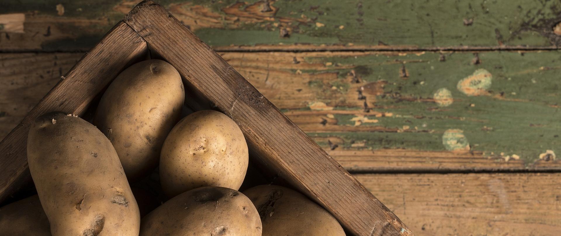Ziemniaki w drewnianej skrzynce stoją na drewnianym podłożu.