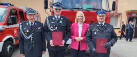 Zdjęcie przedstawia poseł Martę Kubiak komendanta powiatowego Prezesa oraz jednego z druhów na tle samochodu strażackiego