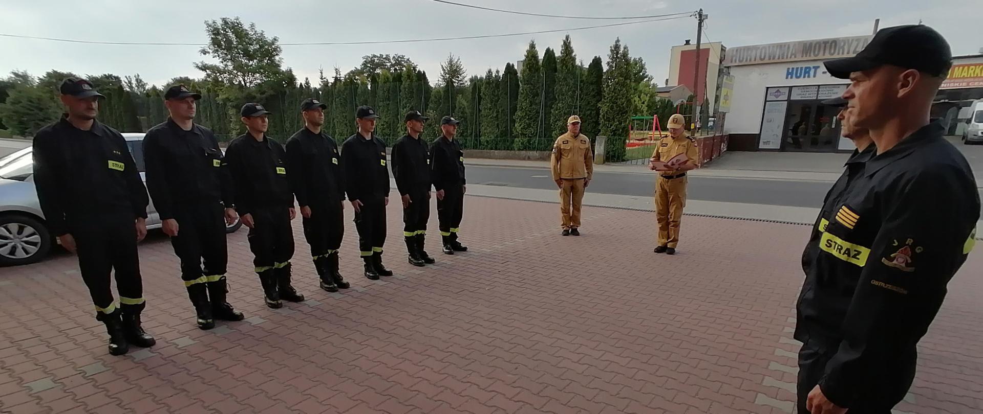 Komendant wręcza nagrodę podczas uroczystej zbiórki na placu manewrowym przed strażnicą.