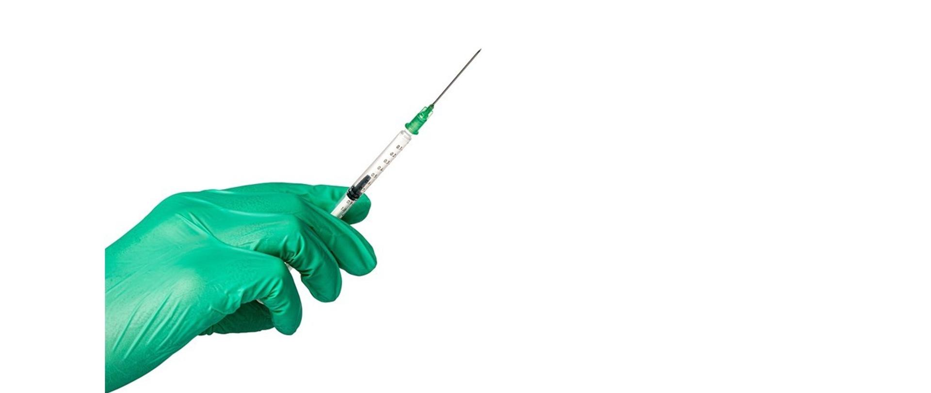 Dłoń w zielonej rękawiczce trzyma strzykawkę