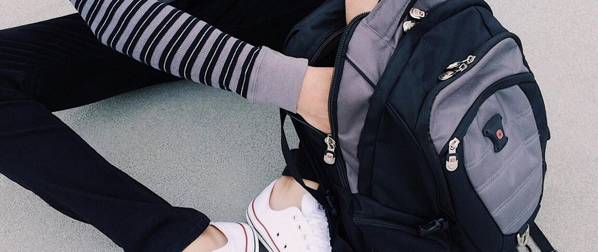 uczeń siedzący na podłodze z otwartym plecakiem