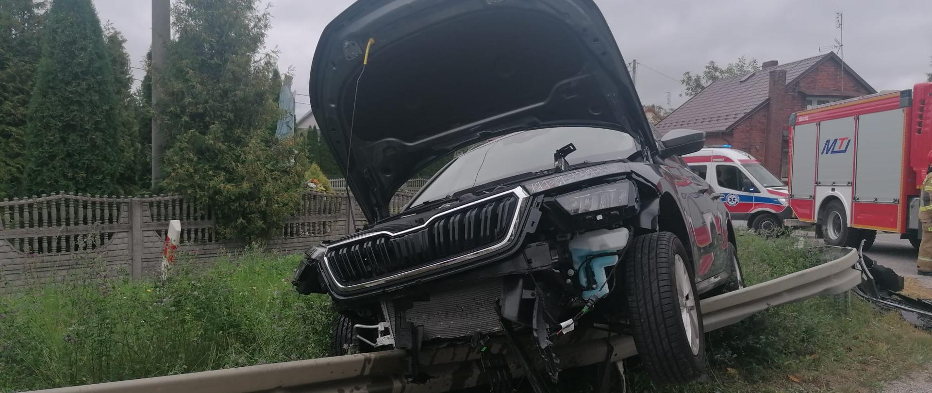 Zdjęcie przedstawia wiszący samochód osobowy na barierach energochłonnych. Na dalszym planie ZRM oraz samochód JOP