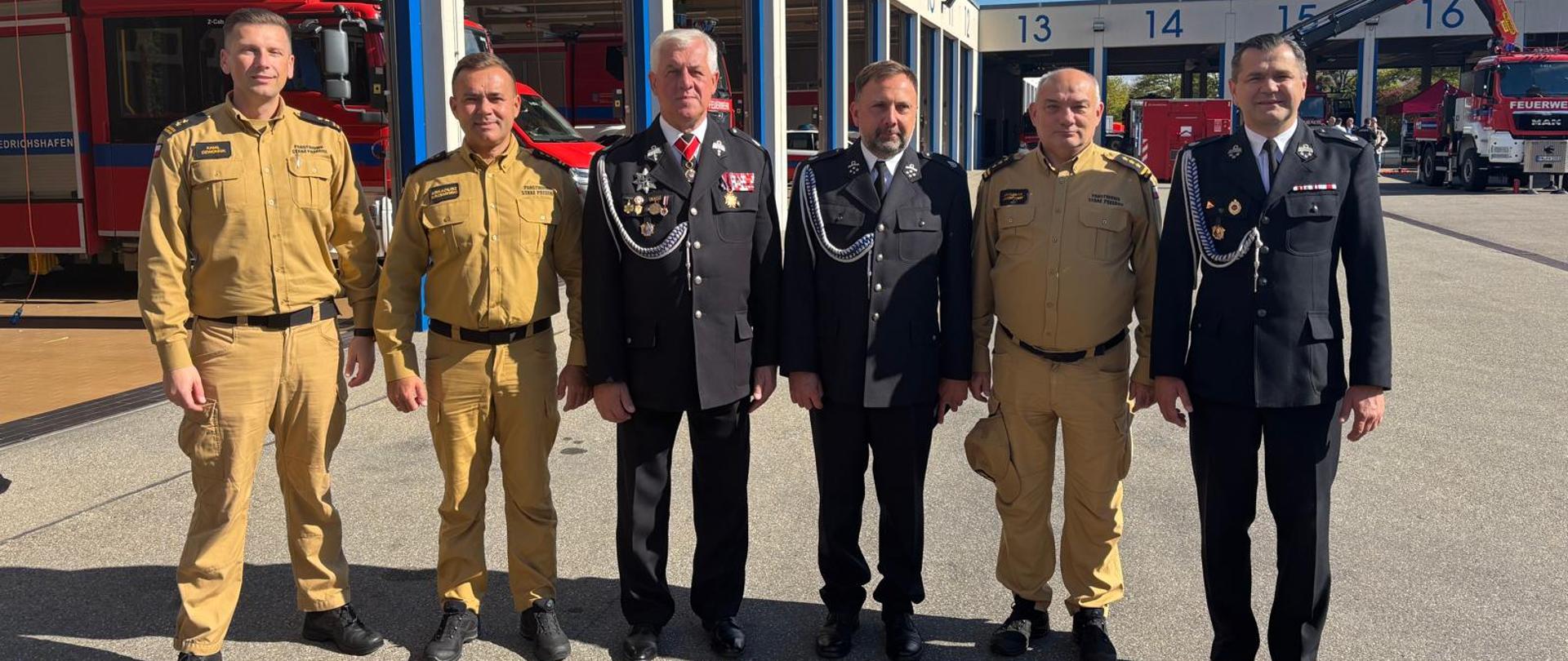 Sześciu mężczyzn w mundurach na pamiątkowym zdjęciu na tle garaży niemieckiej jednostki ratowniczo-gaśniczej