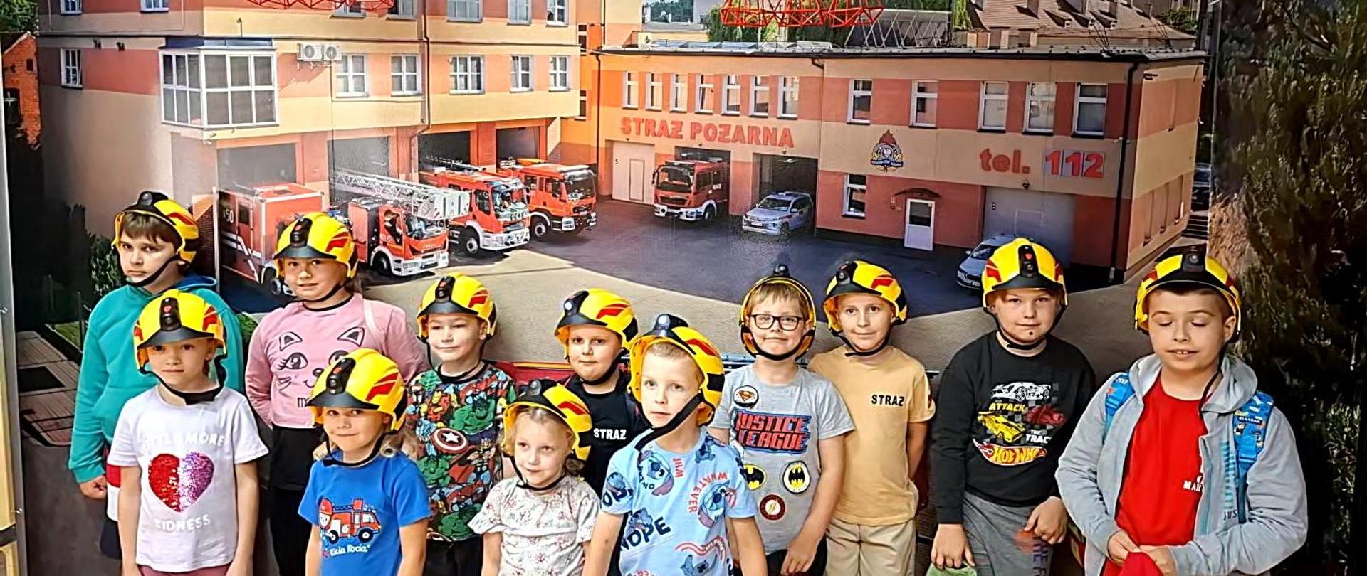 Zdjęcie przestawia strażaków edukujących dzieci.
W tle pomieszczenie Sali edukacyjnej.
