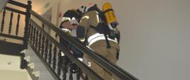 Ćwiczenia w Pakosławiu. Dwóch strażaków wyposażonych w aparaty oddechowe ewakuuje wewnętrzną klatką schodową poszkodowaną pracownicę hotelu. 