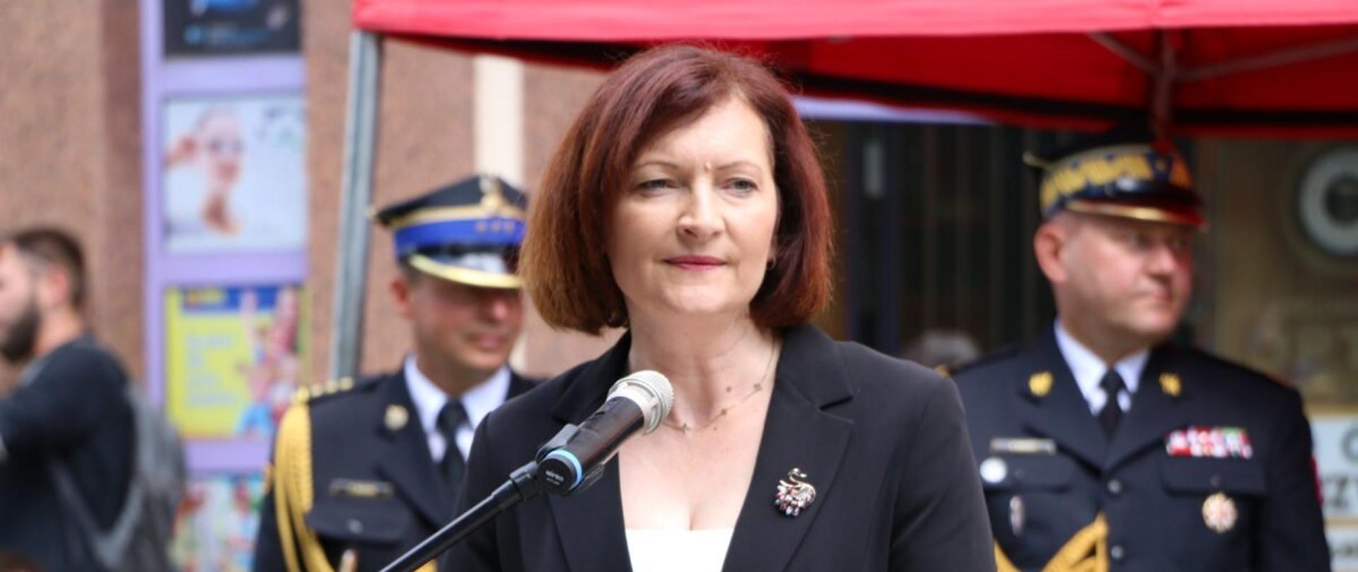 Wojewoda podkarpacki Ewa Leniart przemawia podczas uroczystego apelu z okazji odsłonięcia tablicy pamiątkowej oraz muralu jubileuszowego przy ulicy Mickiewicza 10 w Rzeszowie. W tle strażacy