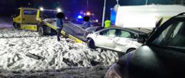 Srebrny pojazd jest ładowany na lawetę, po prawej dwa uszkodzone pojazdy