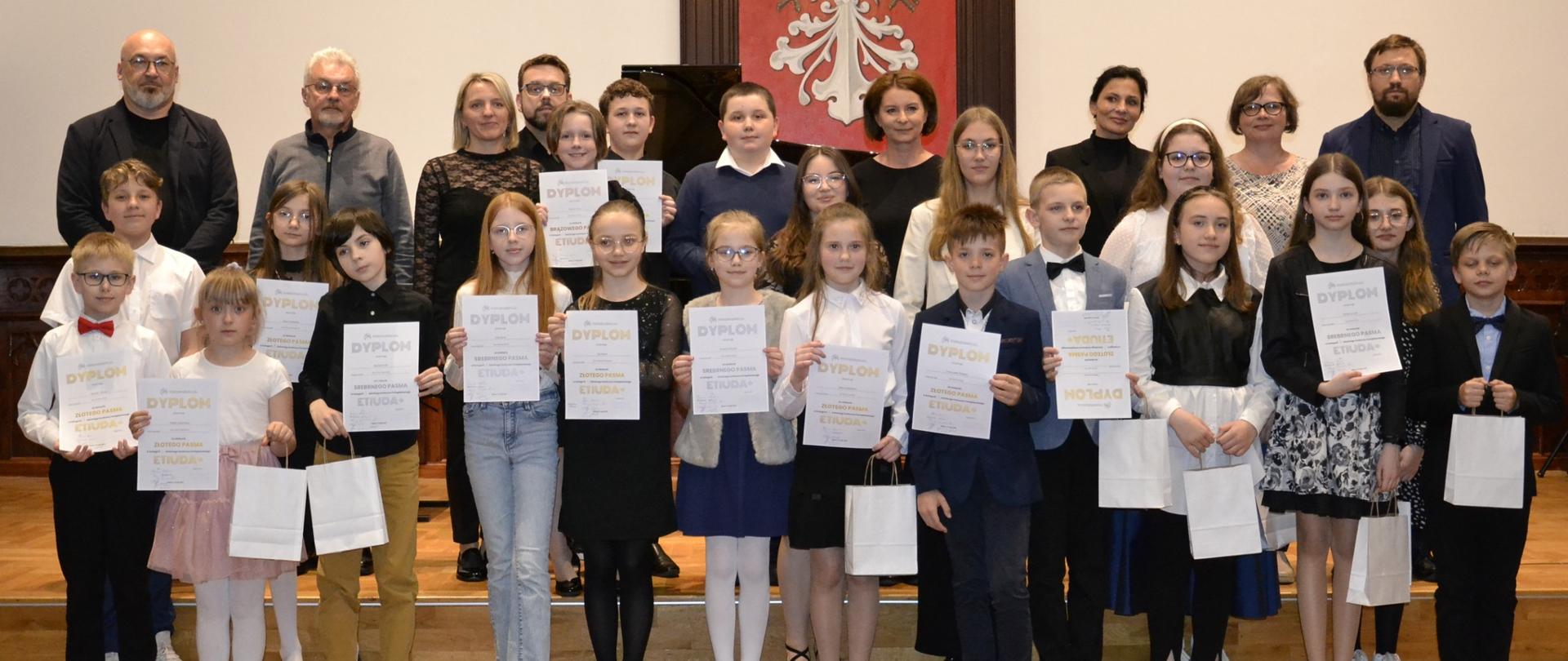 uczniowie fortepianu wraz z nauczycielami podczas Szkolnego Konkursu Fortepianowego "Etiuda+" zgromadzeni na scenie w sali królewskiej PSM MIelec