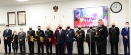 Pomorski komendant wojewódzki Państwowej Straży Pożarnej gratuluje funkcjonariuszom awansów, w tle stoją zaproszeni goście.
