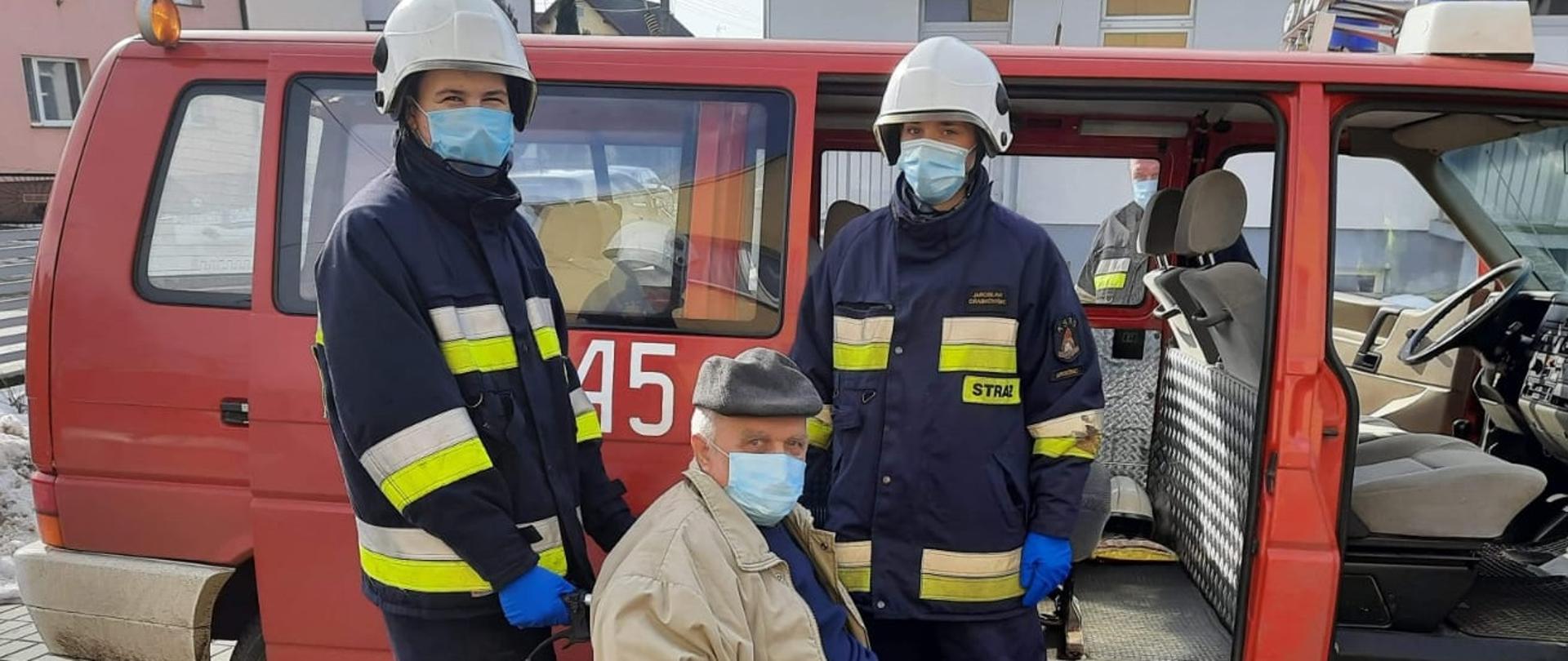 dwóch strażaków OSP i starszy pan na wózku transport na szczepienie