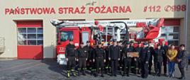 Na zdjęciu widzimy pracowników i funkcjonariuszy Komendy Powiatowej PSP w Pruszczu Gdańskim pozujących na tle podnośnika strażackiego i budynku Komendy podczas pamiątkowego zdjęcia z emerytem.