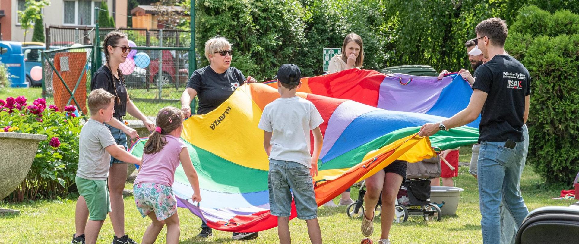 Dzieci oraz młodzież ze Studium podczas pikniku. W rękach trzymają chustę animacyjną. 