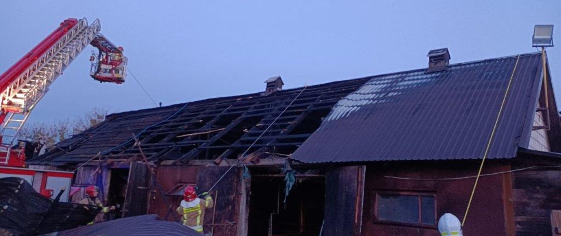 Strażacy przy użyciu podnośnika zabezpieczają dach spalonego budynku