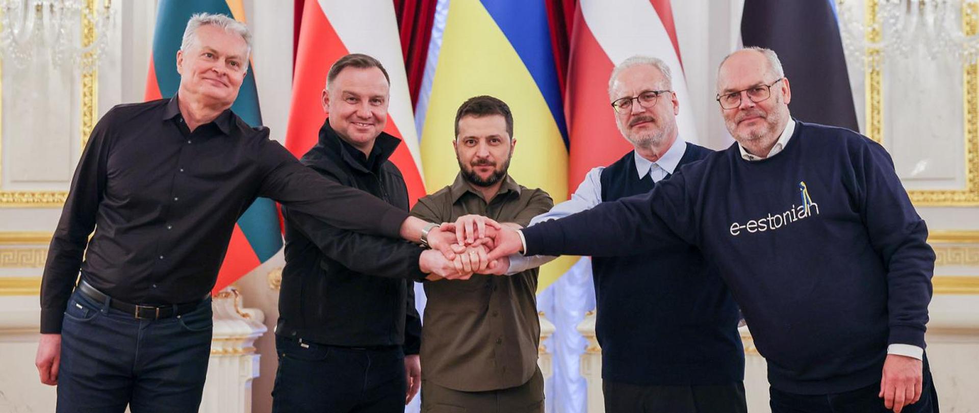 Prezydent Zełenski w otoczeniu innych prezydentów, którzy trzymają dłonie na jego dłoni w geście solidarności