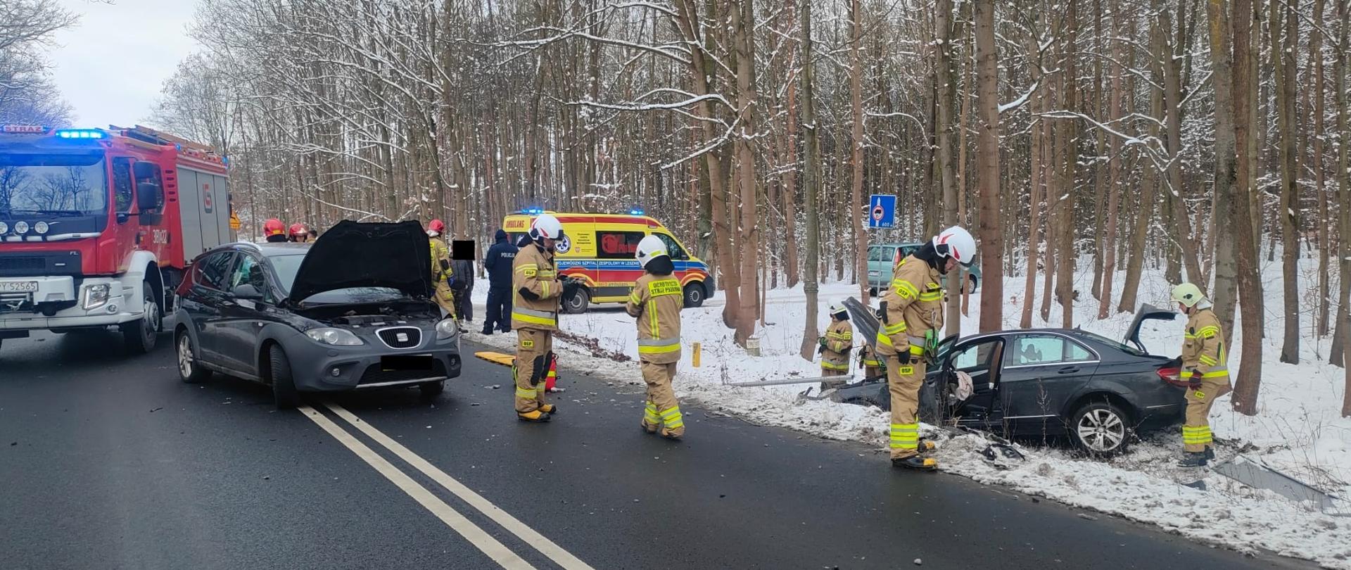 Uszkodzony samochód osobowy stoi w rowie przy lesie na drodze stoi uszkodzony samochód osobowy i pojazdy ratownicze i ratownicy.