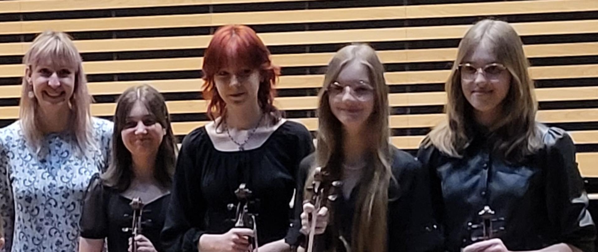 Kobieta i cztery nastolatki stoją w jednym rzędzie na scenie sali koncertowej PSM, wszystkie uczennice trzymają z przodu altówki i smyczki.