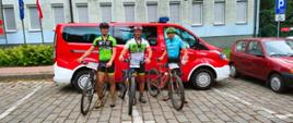 Męszczyźni w strojach sportowych stoją przy rowerach na tle pojazdu strażackiego.