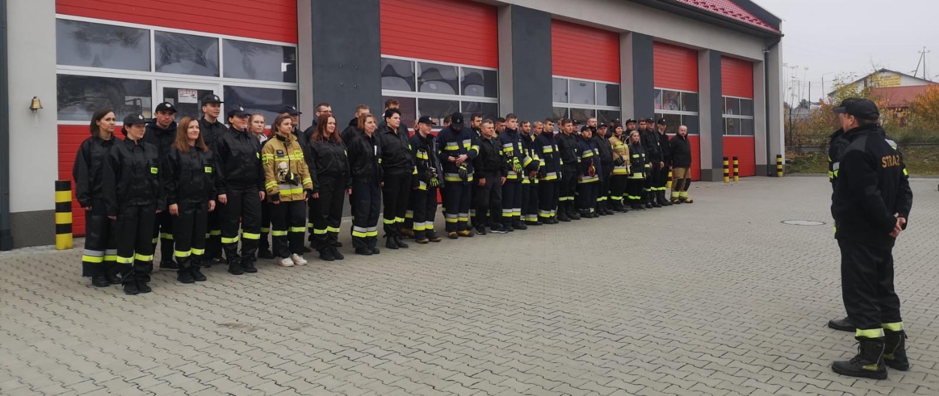 Zdjęcie grupowe przedstawiające wszystkich uczestników kursu podstawowego dla strażaków ochotników ustawionych na tle budynku jednostki w Chmielniku.