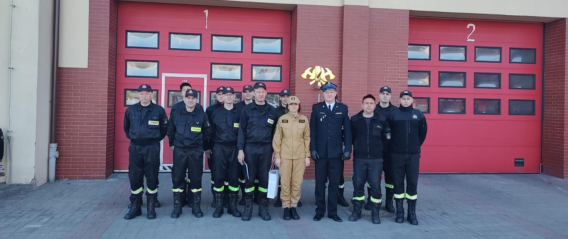 Funkcjonariusze Komendy Powiatowej Państwowej Straży Pożarnej w Rypinie stoją ustawieni do zdjęcia grupowego, na placu wewnętrznym komendy. W tle bramy wyjazdowe garaży jednostki ratowniczo-gaśniczej. Na środku stoi aspirant sztabowy Krzysztof Filipski, który obchodzi trzydziestolecie służby i pracy. Po prawej stronie stoi zastępca komendanta powiatowego Państwowej Straży Pożarnej w Rypinie młodszy kapitan Marcin Czarnecki.