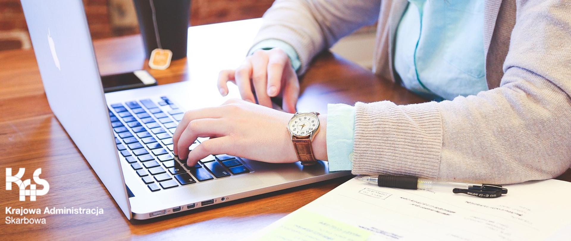 Kobieta przy laptopie, obok kubek z herbatą i książka