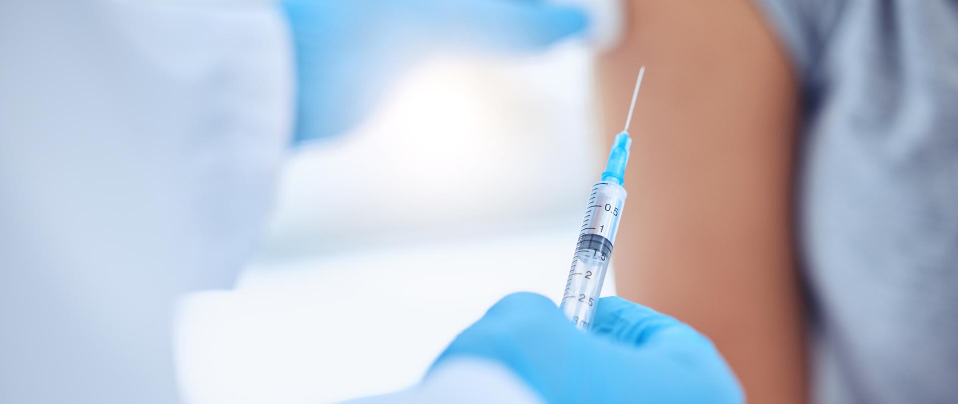 dłoń w rękawiczce ze strzykawką