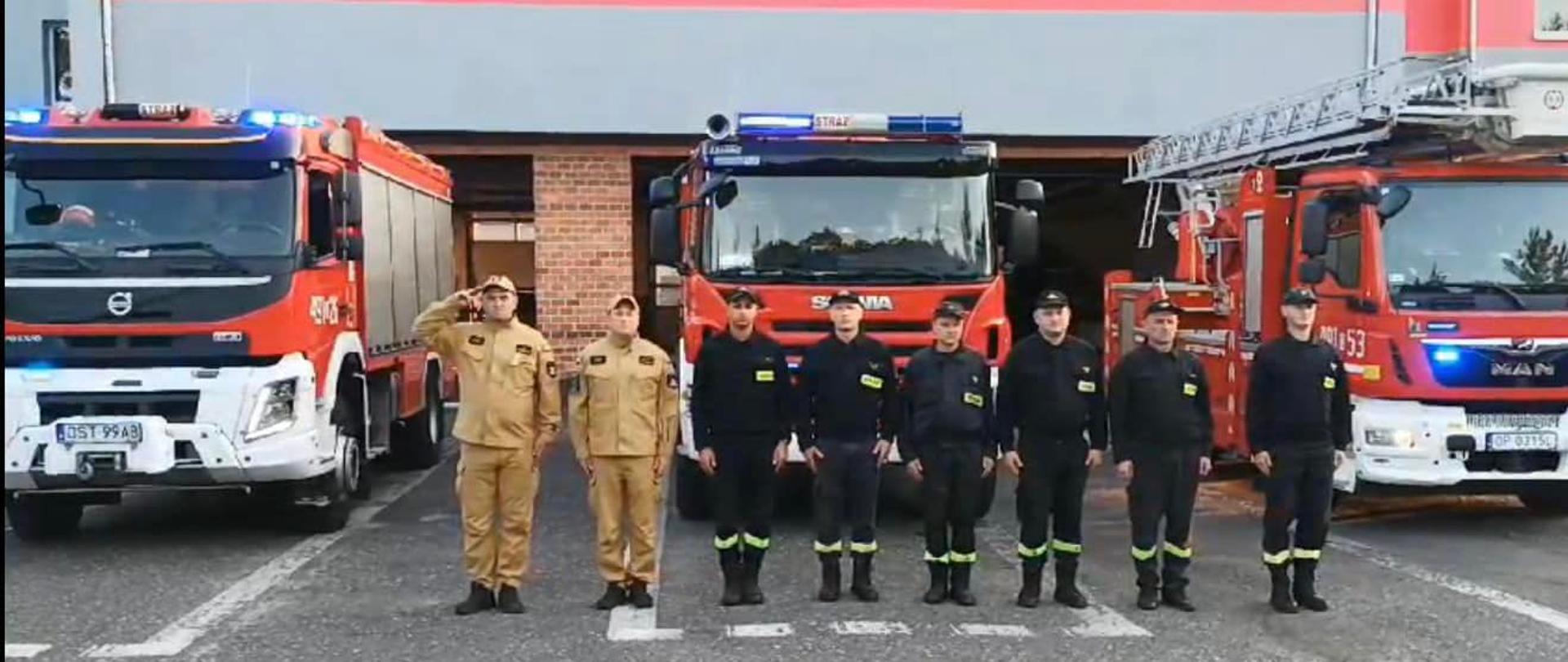 Na zdjęciu znajdują się strażacy ustawieni obok samochodów pożarniczych oddający hołd zmarłemu strażakowi