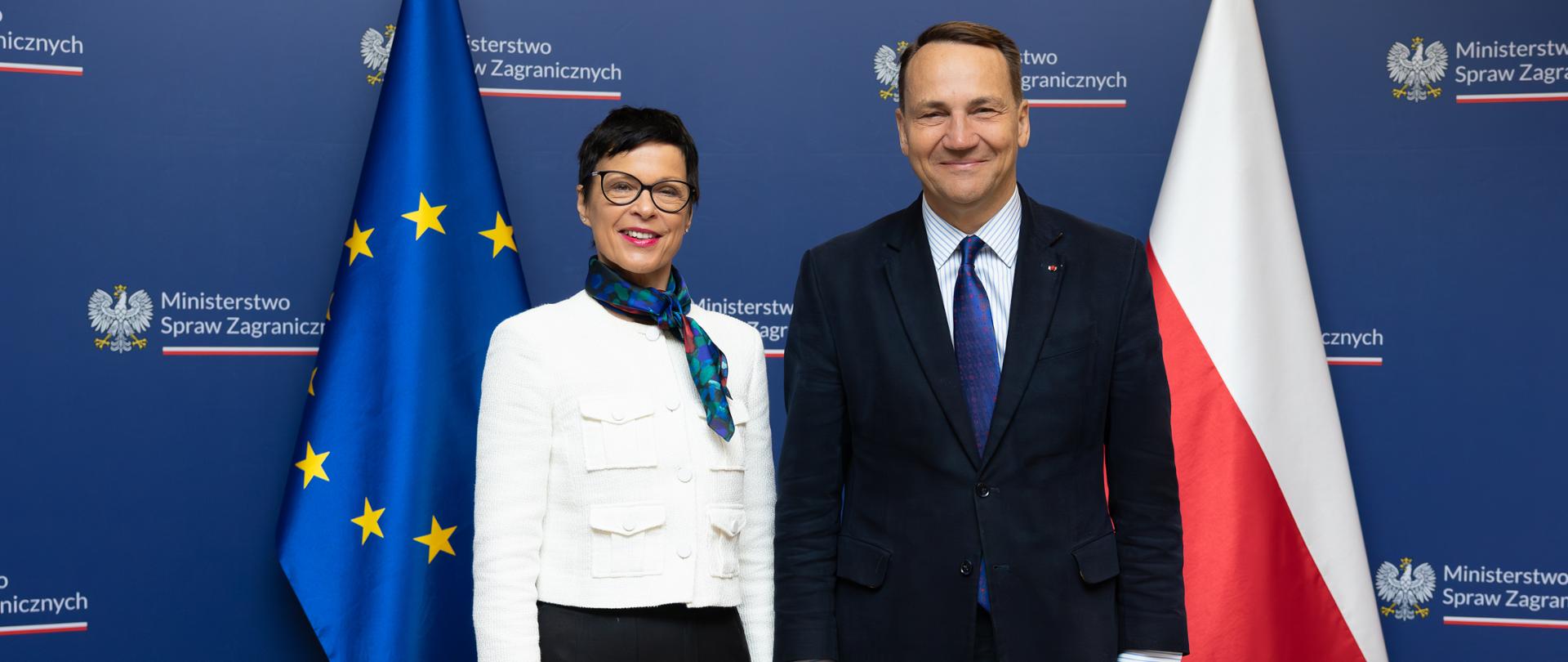 Minister Radosław Sikorski z unijną Komisarz ds. Rozszerzenia Martą Kos na tle flag Unii Europejskiej i Polski

