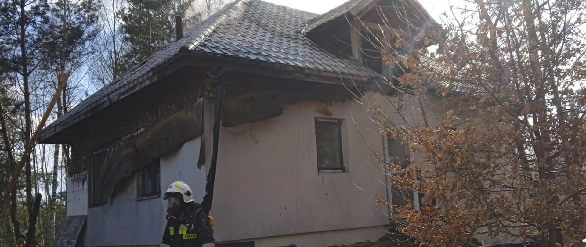 Zdjęcie przedstawia jednorodzinny budynek mieszkalny w którym wybuchł pożar . Elewacja stopiła się a pokrycie dachowe zdeformowało z powodu zniszczenia więźby.