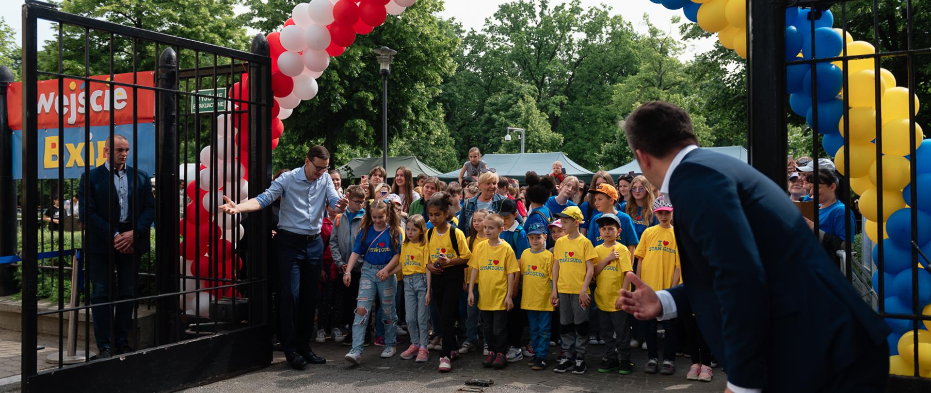 Premier Mateusz Morawiecki otwiera bramę do KPRM przez którą wchodzą dzieci