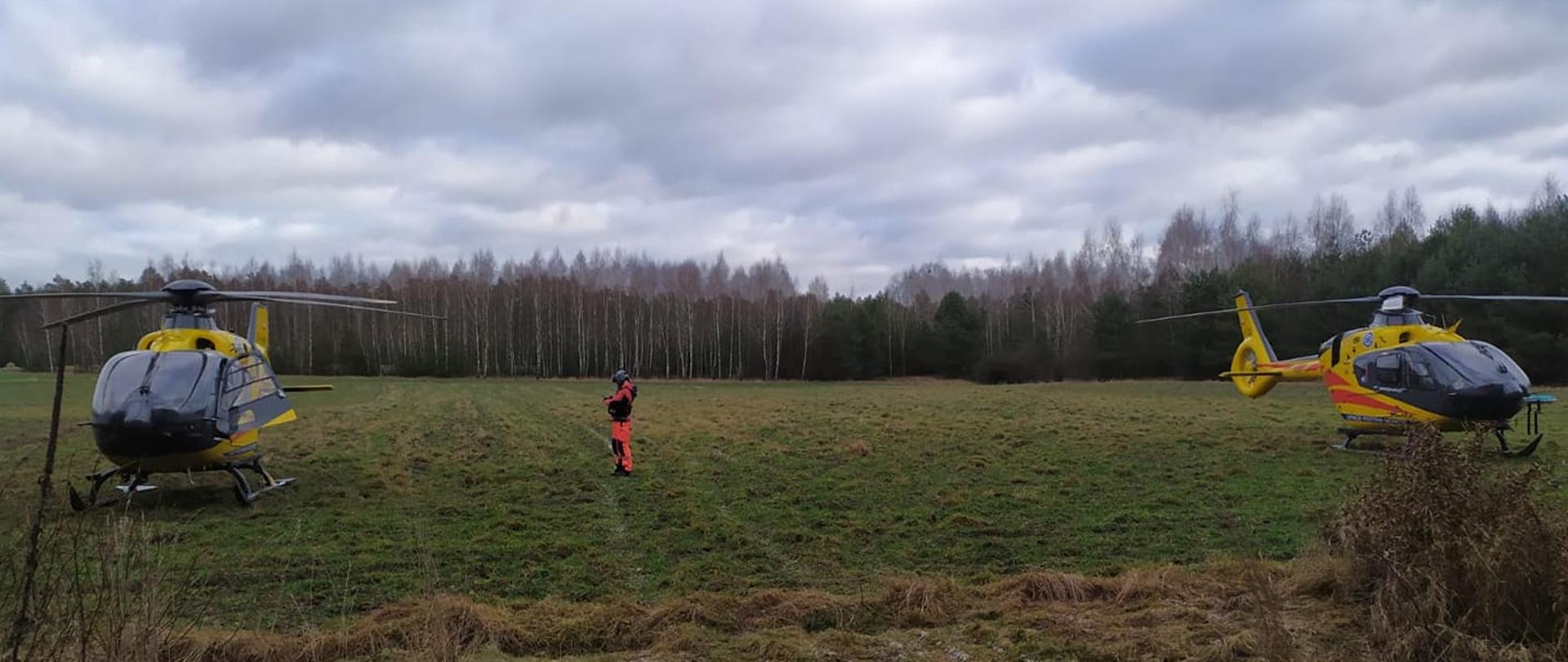 Dwa śmigłowce LPR wylądowały na łące. Pomiędzy nimi stoi ratownik.